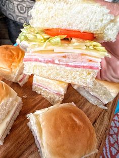 a person is holding a sandwich on a cutting board with several different types of sandwiches