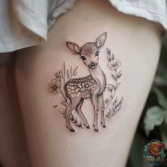 a small deer tattoo on the side of a woman's thigh, with flowers around it