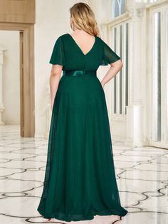 a woman in a long green dress standing on a marble floor with her back to the camera