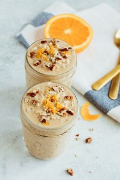 two glasses filled with oatmeal sitting next to an orange slice