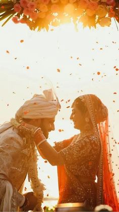 two people standing next to each other under a flower covered canopy with petals flying around them