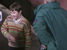 a young boy in a colorful sweater is talking to an older man