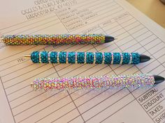 three pens sitting on top of a piece of paper with some colored beads in them