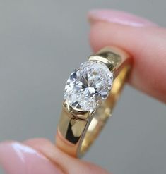 a woman's hand holding a yellow gold ring with a white diamond in it