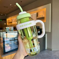 a person holding up a green cup with ice cream on it in front of a store