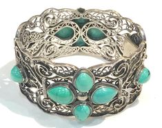 This beautiful vintage BJ   sterling silver hinged oblong shaped bangle  features a wide textured sterling filigree with bezel set with 12 pear shaped turquoise cabochon flower shapes on both sides.   The bracelet measures 7" inner circumference and 1.25" W and has a tongue and groove clasp and is in very good to excellent vintage condition with the turquoise nice, light tarnish.  Hallmarked BJ 925 China and weighs 58 grams Shipping prices vary on the weight of item. I do my best to keep shippin Ornate Turquoise Jewelry For Collectors, Turquoise Bangle For Formal Occasions, Formal Turquoise Bangle Jewelry, Ornate Turquoise Jewelry For Wedding, Antique Turquoise Bangle, Ornate Turquoise Filigree Jewelry, Carved Bangle Jewelry, Vintage Turquoise Jewelry With Intricate Design, Ornate Hinged Jewelry Bracelet