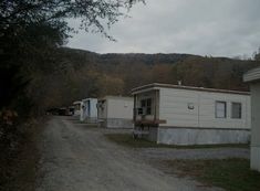 several mobile homes are lined up along a dirt road in front of a wooded area