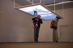 three people are standing in front of a projection screen with clouds on it and one person is holding a child