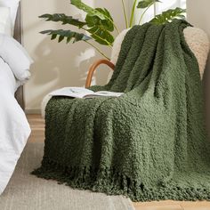 a green blanket sitting on top of a bed next to a chair and potted plant