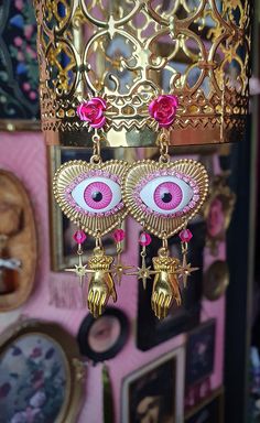 A mystical all seeing eye stud dangle earring in gold an pink. The earrings measure: Width(widest part): 3cm Height: 7cm Pink Teardrop Jewelry For Festivals, Pink Dangling Charms Drop Earrings, Pink Dangle Earrings With Charms, Pink Drop Earrings With Dangling Charms, Party Dangle Evil Eye Jewelry, Mystical Gold Earrings For Festival, Pink Bohemian Jewelry With Evil Eye Detail, Pink Metal Pierced Jewelry, Pink Evil Eye Spiritual Jewelry