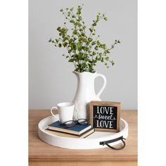 a white vase filled with green plants on top of a wooden table next to a book