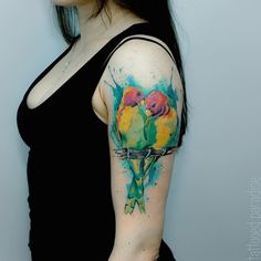 a woman wearing a black top with colorful birds on her arm and shoulder tattoo design