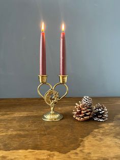 two candles are sitting next to each other on a wooden table with pine cones in the background