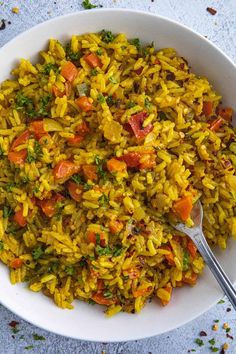 a bowl filled with rice and carrots on top of a blue tablecloth next to a spoon