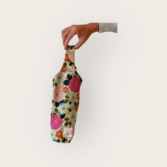 a hand holding a floral fabric covered wine bottle