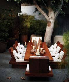 an outdoor dining table with candles on it and some chairs around it, in front of a tree