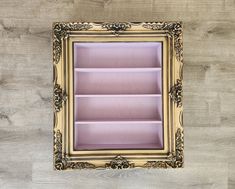 a gold frame with pink shelves in the middle on a wood flooring wall behind it