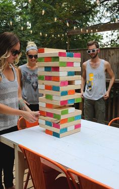 three people standing around a table with a giant block tower on it's side