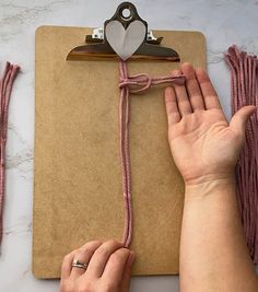 two hands are holding a clipboard with pink cords and a heart shaped paperclip