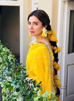 a woman with long hair wearing a yellow dress and flowers in her hair, standing on a balcony