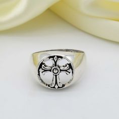 a silver ring with a cross on the front and center, sitting next to flowers