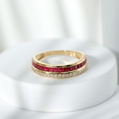 a gold ring with red and white stones on it sitting on top of a white surface