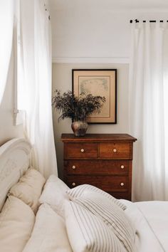 a bedroom with a bed, dresser and white curtains