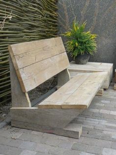 a wooden bench sitting on top of a brick floor next to a potted plant