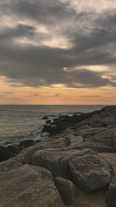 a bench sitting on top of a rocky beach next to the ocean under a cloudy sky