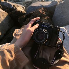 a person holding up a camera to take a photo on the rocks by the water