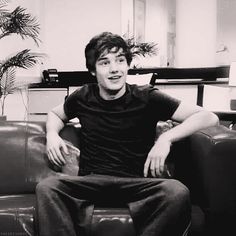 a young man sitting on top of a couch next to a potted palm tree