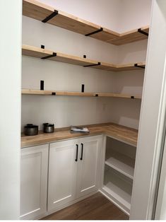 an empty pantry with wooden shelves and white cupboards