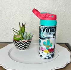 a cactus and some succulents sit on a plate next to a cup