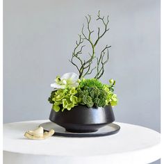 a white table topped with a black vase filled with flowers and greenery on top of it