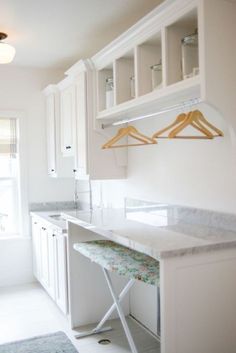 an empty kitchen with white cabinets and marble counter tops, along with hanging clothes rails