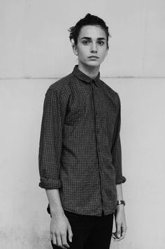 a young man standing in front of a white wall wearing a shirt and black pants