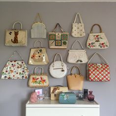 many purses are hanging on the wall above a white dresser in a living room