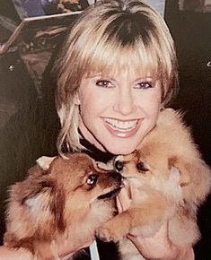 a woman holding two small dogs in her arms and smiling at the camera with other dogs behind her