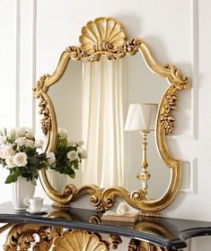 an ornate gold framed mirror on a black table with flowers and vases in front of it