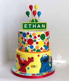 a birthday cake with sesame street characters and balloons on the top tier is decorated in bright colors