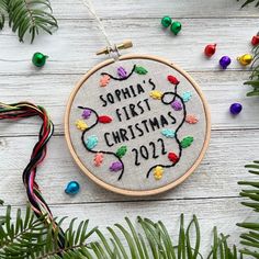 a cross stitch christmas ornament hanging on a wooden table with ornaments around it