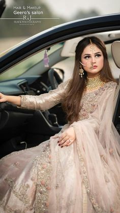 a woman sitting in the driver's seat of a car wearing a dress and jewelry