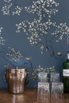 a bottle of wine sitting next to two glasses on top of a wooden table with a tree painted on the wall behind it