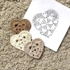 three crocheted hearts sitting on top of a piece of paper next to an envelope