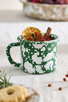 a green and white mug filled with cinnamons, orange slices and other food items