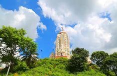 a very tall building sitting on top of a lush green hillside under a blue cloudy sky