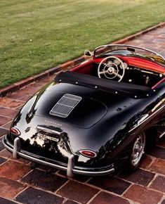 an old fashioned black sports car parked on the side of a brick road with grass in the background