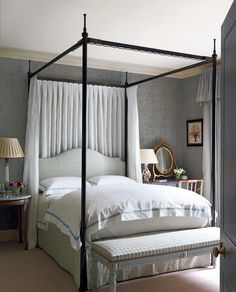 a four poster bed with white sheets and pillows