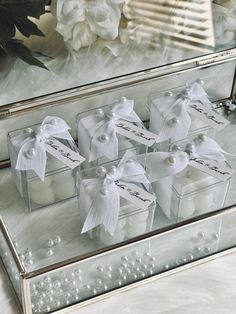 four small boxes with white candles in them on a table next to flowers and pearls