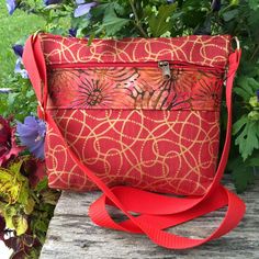 a red purse sitting on top of a wooden table next to purple and blue flowers